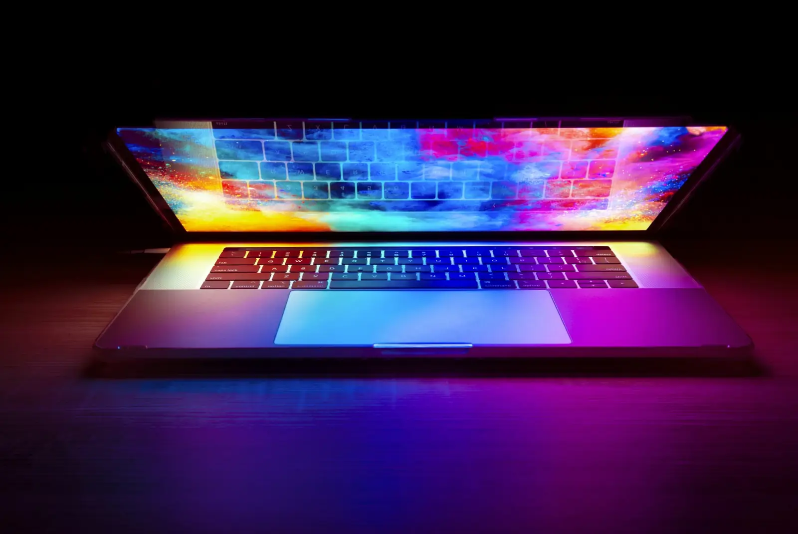 An open laptop glowing with bright colours on a dark desk