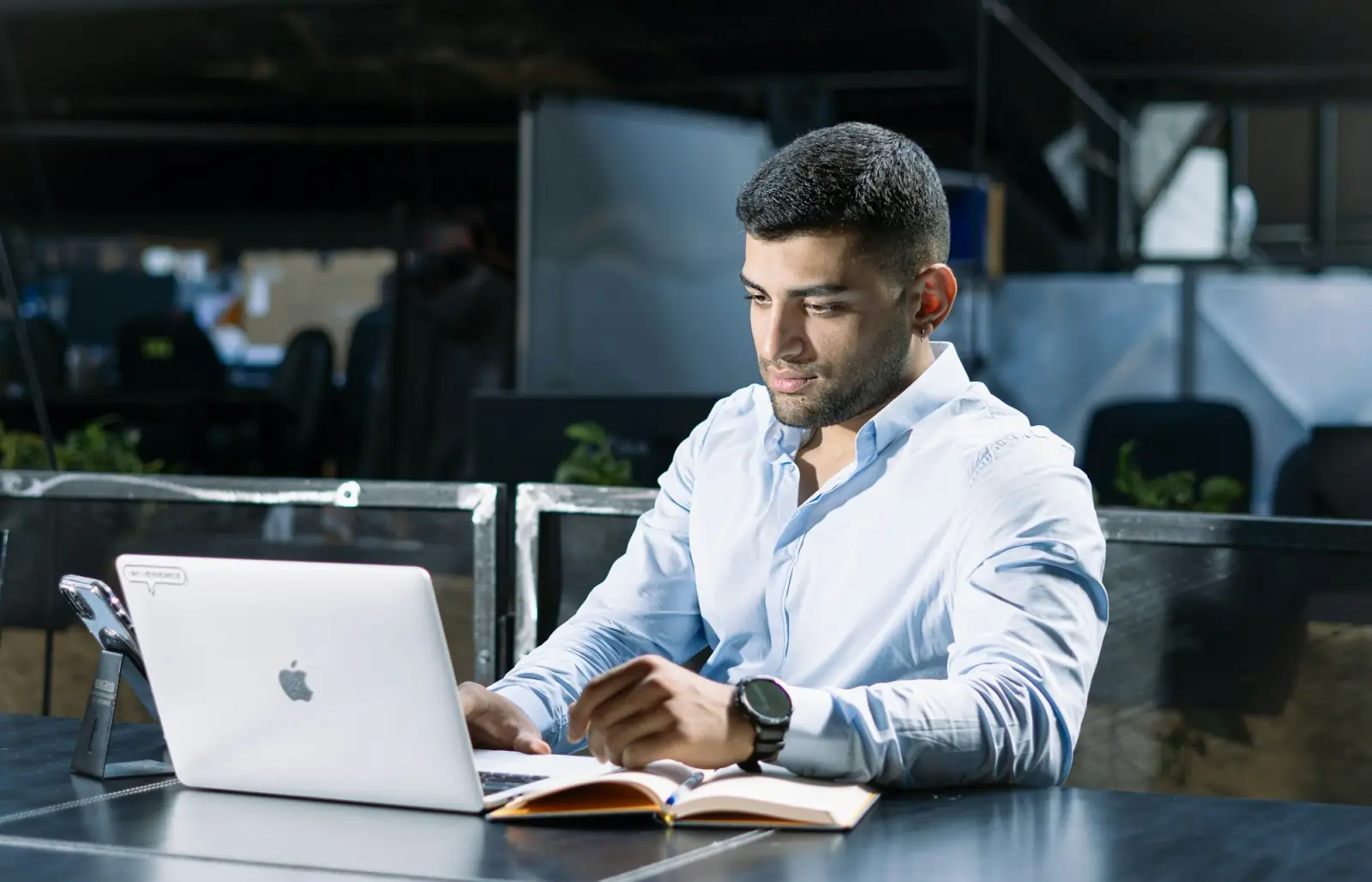 A man typing on a laptop at a light wooden desk against a concrete wall