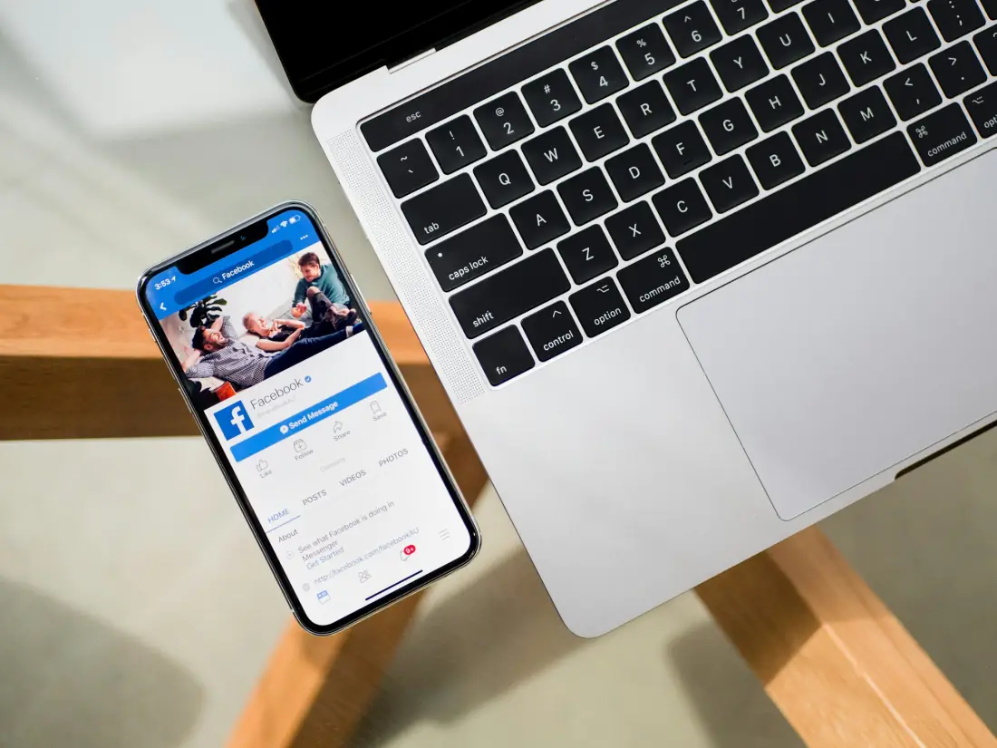A phone showing a social feed beside an open laptop on a wooden table