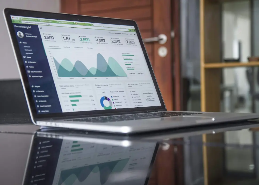 A laptop on a glass desk showing a business dashboard with charts and figures